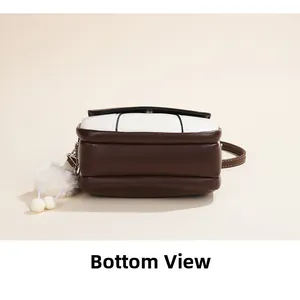 Detail view of the brown leather bottom and white plush keychain on a crossbody bag