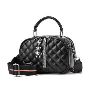 Black quilted crossbody bag with dual zippers and bear pendant on white background