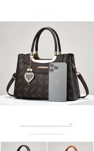 Detail of dark brown tote with logo prints, gold-tone hardware, and heart charm accessory