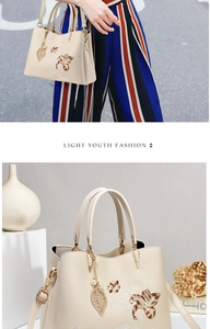 Dettaglio borsa in pelle crema con ricamo floreale ed elegante ciondolo a foglia di perla