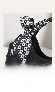 Detail of black pebbled leather handle featuring a checkered heart print silk scarf bow