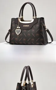 Detail of dark brown leather tote with orange logo print and gold heart pendant