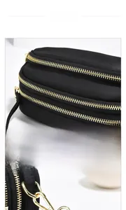 Détails d'un sac bandoulière noir avec trois fermetures éclair dorées et crochets en métal