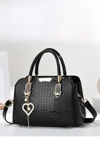 Detail of black crocodile texture handbag with gold hardware and a heart pearl charm
