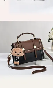 Détail d'un sac à main bicolore marron et noir avec boucle dorée et pendentif peluche