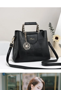 Detail of black leather handbag with patchwork texture and gold floral pendant
