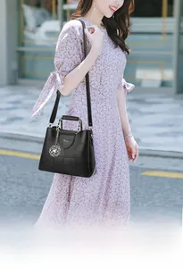 Detail of black faux leather handbag with gold chain handle and white floral charm