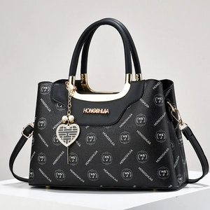 Schwarze Monogramm-Handtasche mit Herz-Perlenanhänger und Griff auf weißem Display