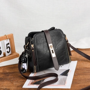 Black vintage square bucket bag with brown leather strap and metal lock on wooden table