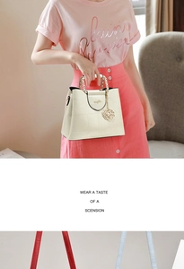 Detail of cream handbag featuring geometric embossing, gold chain, and camellia charm