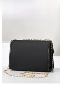 Detail of black quilted shoulder bag featuring white contrast stitching and gold chain strap