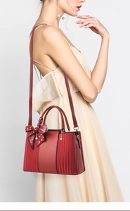 Red leather handbag with silk scarf shown on model wearing champagne pleated dress