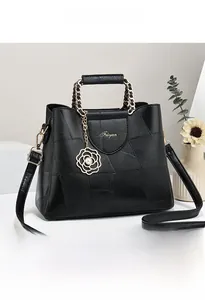 Detail of black leather handbag featuring chain handle and camellia flower pendant