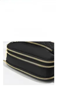 Detail of three-layer golden zipper closure on high-density black nylon crossbody bag