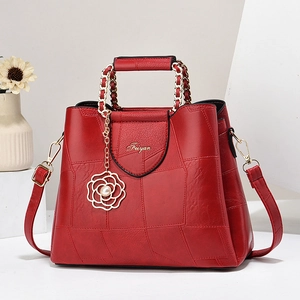 Elegant red leather handbag with gold logo and rose pearl charm on a minimalist white stage