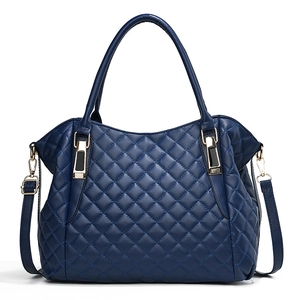 Quilted navy blue leather handbag with dual handles and adjustable shoulder strap on white