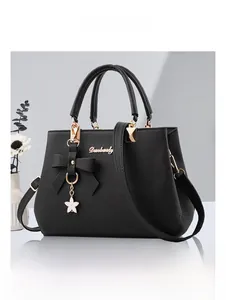 Detail of black litchi grain PU leather tote bag with elegant bow and floral charm