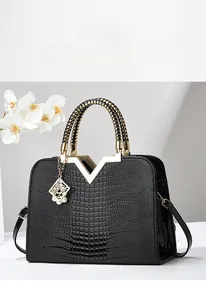 Détail du sac à main noir motif crocodile avec boucle en V dorée et pendentif orné d'une perle