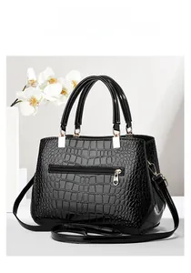 Detail of elegant black crocodile pattern handbag with golden metal link hardware and strap