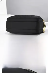 Macro detail of black quilted nylon bag showing double gold zippers and stitching