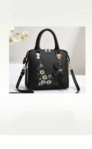 Detail of black faux leather handbag featuring floral embroidery and butterfly charm