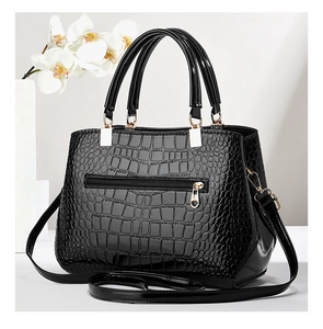 Detail of black glossy crocodile embossed leather handbag with elegant gold hardware