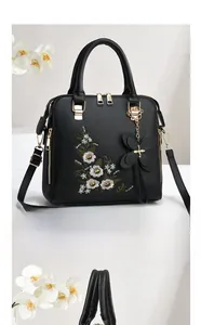 Detail of floral embroidery and butterfly pendant on a black faux leather tote bag