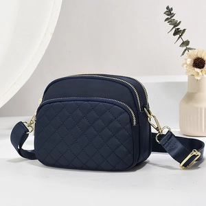 Navy blue nylon crossbody bag with quilted pockets and three gold zippers on a clean setup