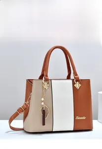 Detail einer dreifarbigen Handtasche mit Quastenanhänger und verstellbarem Schultergurt