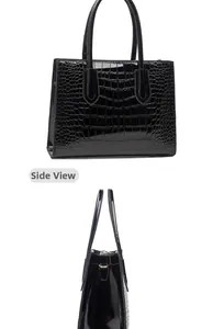 Detail view of the side and front of a glossy black crocodile pattern tote bag with handles
