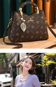 Detail of printed crossbody bag with gold metal handle and leaf pendant on wooden surface