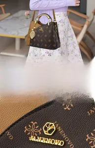 Detail of monogram leather tote with gold metal handles and elegant leaf pendant decoration