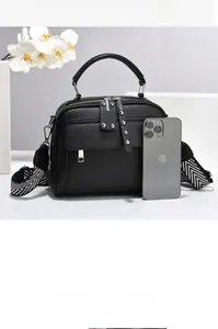 Detail of black pebbled leather handbag with wide geometric strap and iPhone size reference