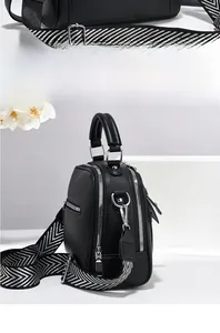Detail of black pebbled leather tote bag with silver zippers and chevron fabric strap
