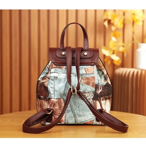Detail of a fashion backpack with denim texture and brown leather straps on a wooden table
