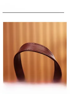 Close-up of the durable leather top handle featuring fine stitching on a dark red backpack