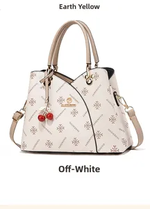 Detail of cream leather handbag featuring printed patterns and cherry bag charm