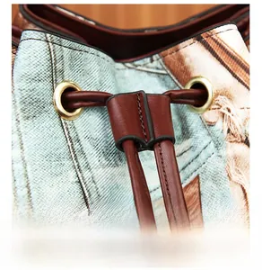 Detail of blue denim canvas bucket bag featuring brown leather drawstring and golden eyelets
