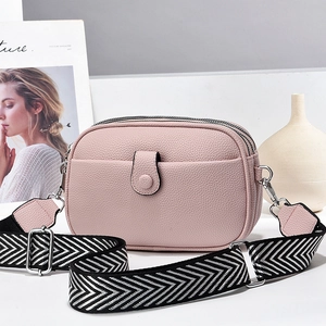Pink lychee grain leather crossbody bag with triple zippers and woven strap displayed on a desk