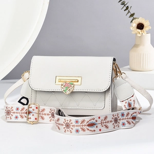 Elegant white crossbody bag with gold heart clasp and floral embroidered strap