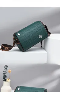 Detail of dark green crocodile texture cylinder bag with brown clover pattern strap