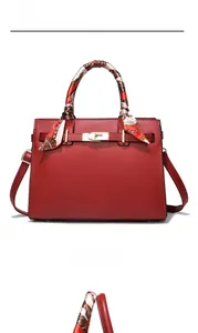Detail of red leather handbag featuring gold buckle hardware and decorative silk scarf