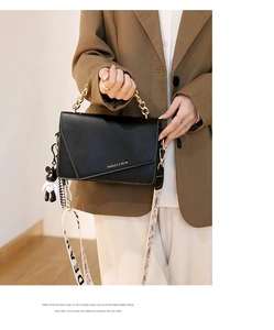 Detail of black crossbody bag with gold chain handle and wide graphic shoulder strap
