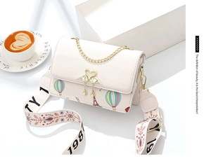Detalle de bolso crema con solapa, hebilla de cisne dorado y borla de perlas en mesa blanca