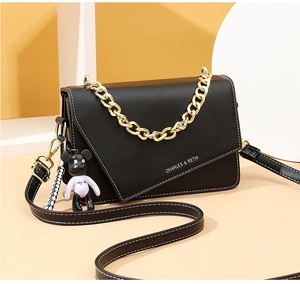 Detail of black crossbody bag with asymmetric flap, white stitching, and panda bear charm