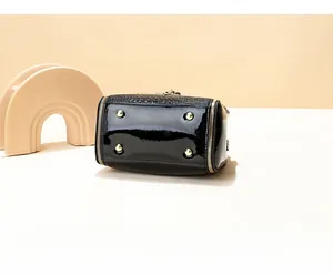 Detail view of glossy black bucket bag bottom featuring four protective gold metal studs