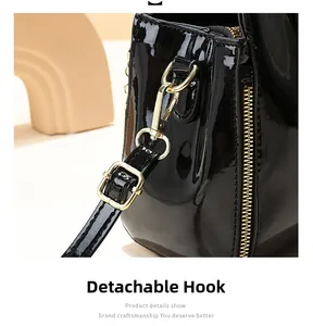 Detail of black patent leather bucket bag featuring gold metal hook and zipper hardware