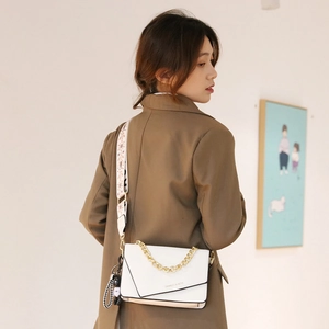 Chic white leather crossbody bag with gold chain and printed strap on a female model