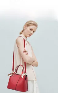 Detail of red leather handbag with lychee grain texture and decorative silk scarf handle