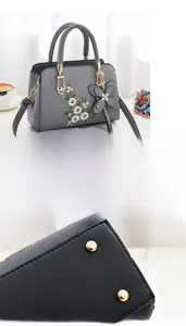 Detail view of colorful floral embroidery and golden base rivets on a gray leather handbag